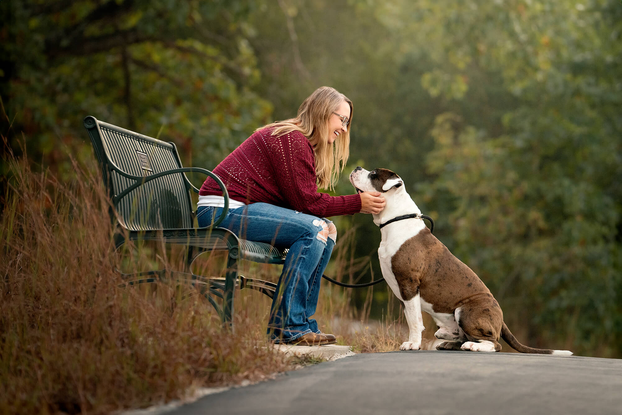 blonde dog owner sitting on a bench, leaning down to scratch her dog's chin